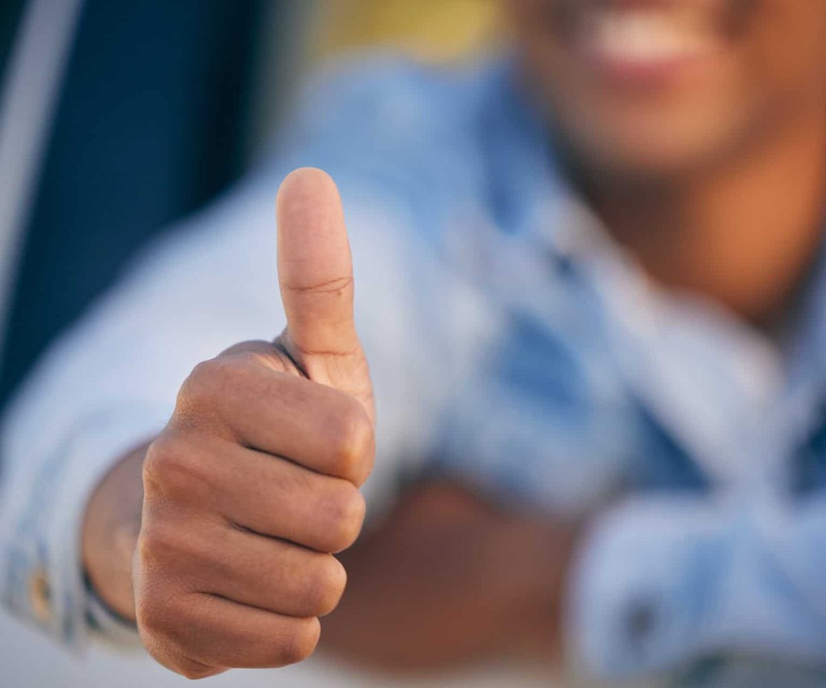 Shot of an unrecognisable man showing thumbs up while traveling in a car.