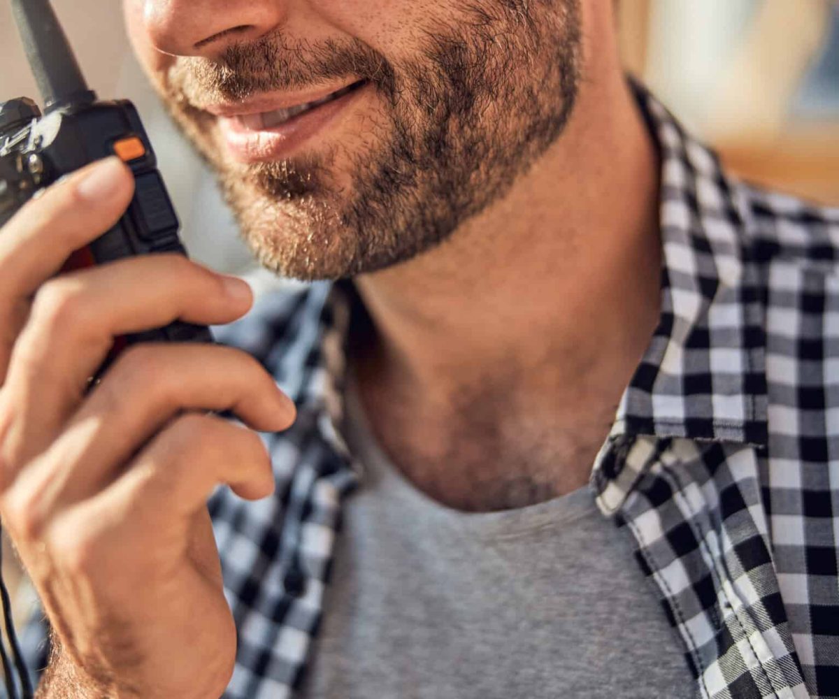 Cropped photo of a bearded young man in a checked shirt holding a walkie-talkie to his mouth